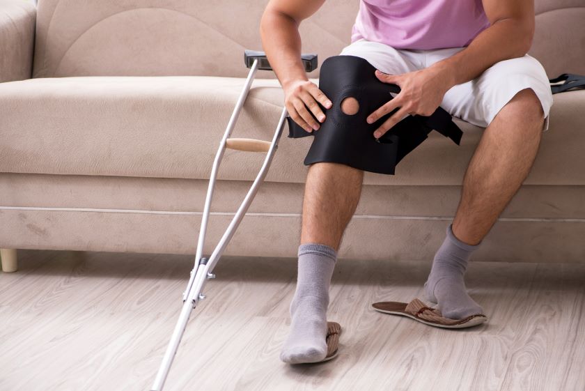 Man sitting on a couch with a crutch and knee brace